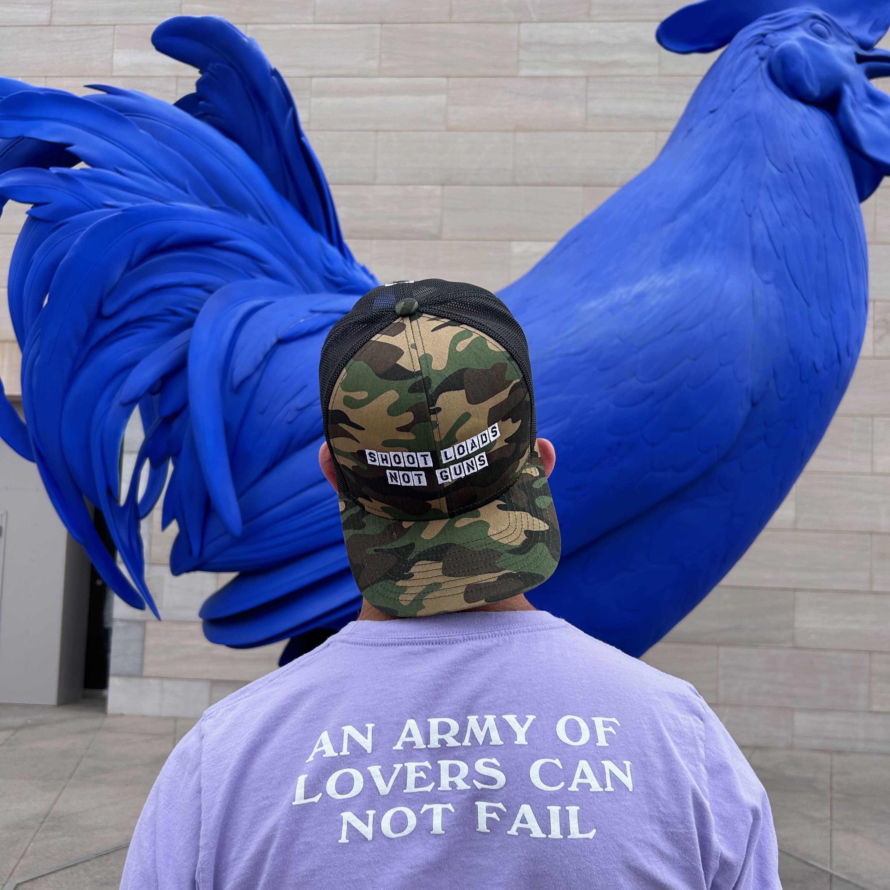 Person wearing a cap and t-shirt with text, standing next to a large blue sculpture.