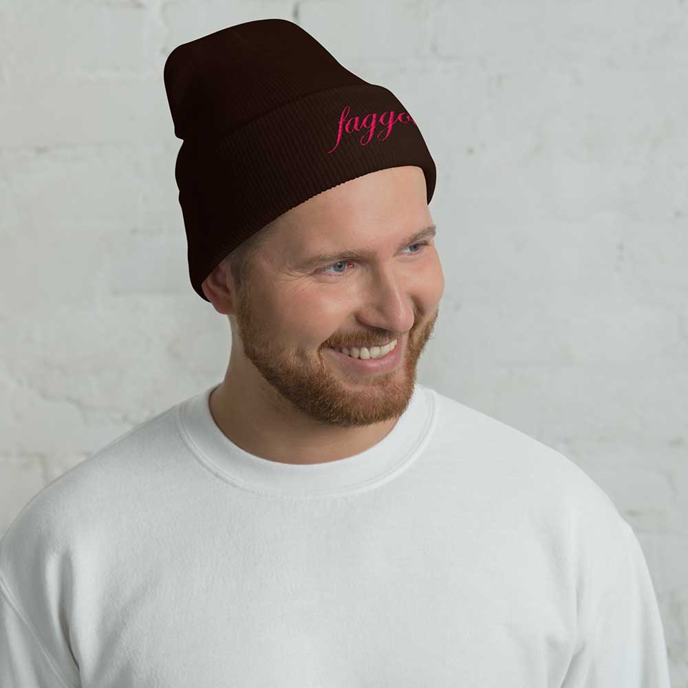 Man wearing a brown beanie with pink faggot text against a light gray background
