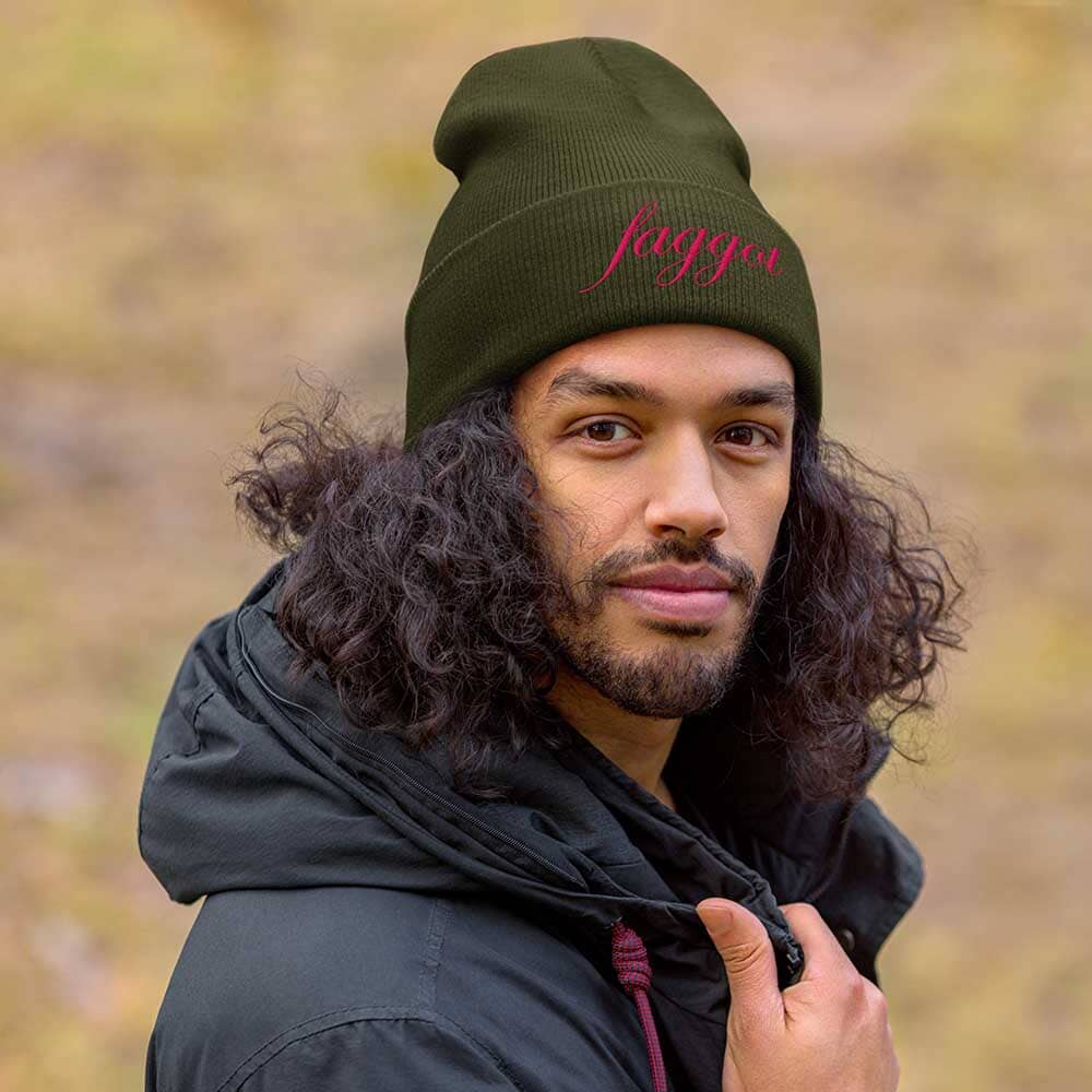 Person wearing a green beanie with 'faggot' branding against a blurred natural background
