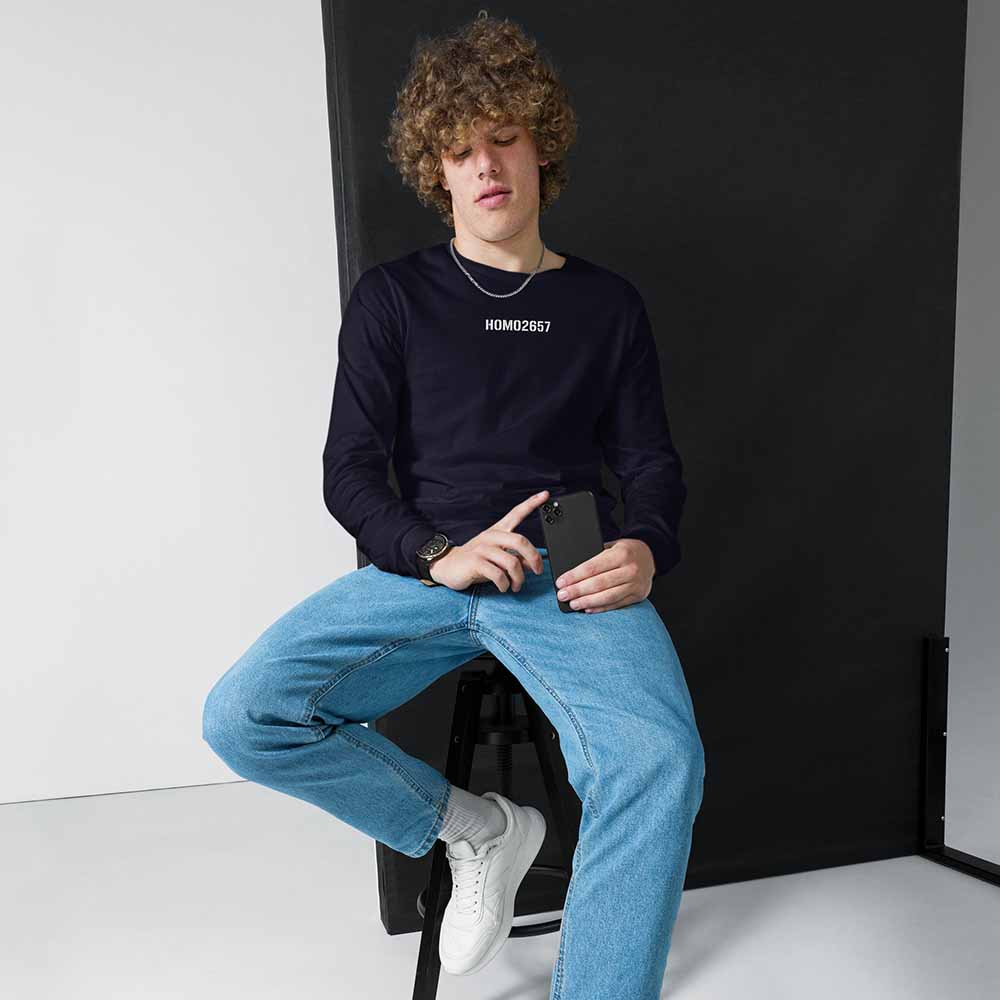 Person sitting on a black stool holding a phone, wearing a navy long sleeve t-shirt and light blue jeans.