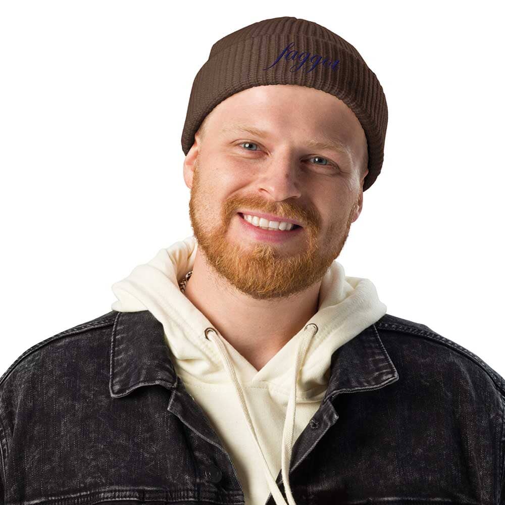 Man wearing a brown beanie with 'faggot' embroidery, a black jacket, and a white hoodie on a white background.
