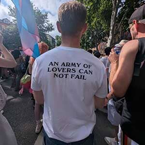 Person wearing a white t-shirt with 'An Army of Lovers Can Not Fail' text at a public event.