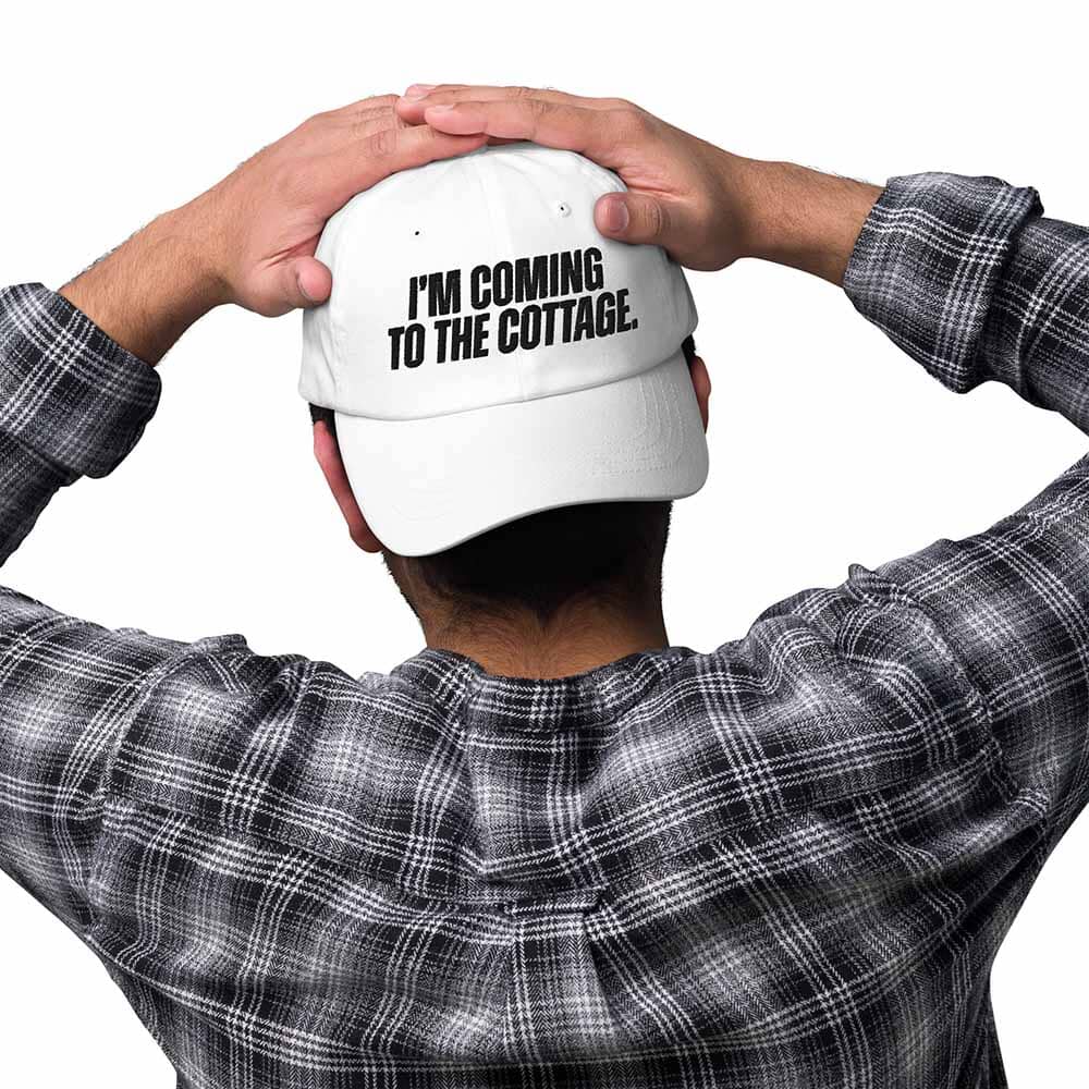 Person wearing a white cap with text 'I'm coming to the cottage' on a white background