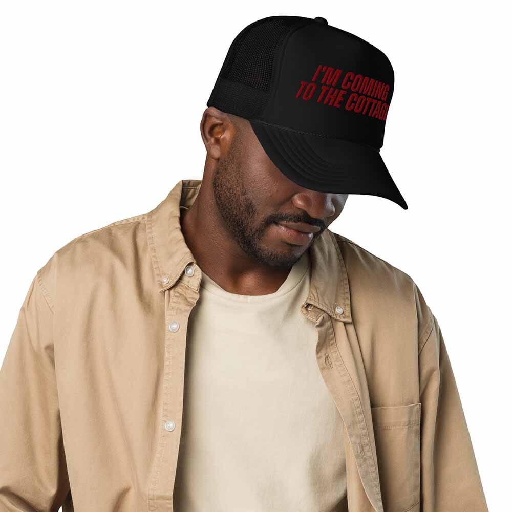 Man wearing a black cap with red text and a beige jacket on a white background