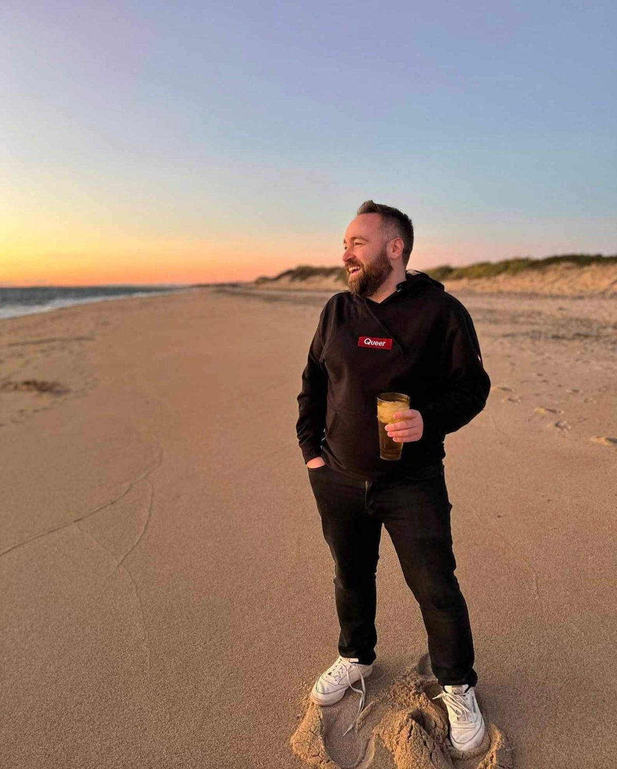 A customer on a Provincetown beach at sunset in the black Queer hoodie