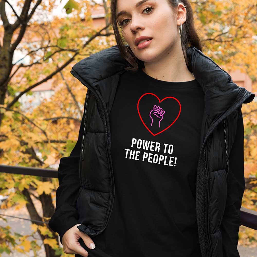 Person wearing a black t-shirt with a heart and hand design, text 'Power to the People!' in an outdoor setting with autumn leaves.