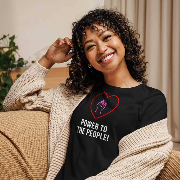 Woman wearing a black shirt with a heart and hand design, sitting on a couch.